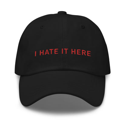 Bild eines Baseball-Caps mit dem Spruch 'I HATE IT HERE' auf weißem Hintergrund. Ein humorvolles Accessoire für diejenigen, die lieber zuhause bleiben. Hergestellt aus Baumwoll-Chino-Cord.