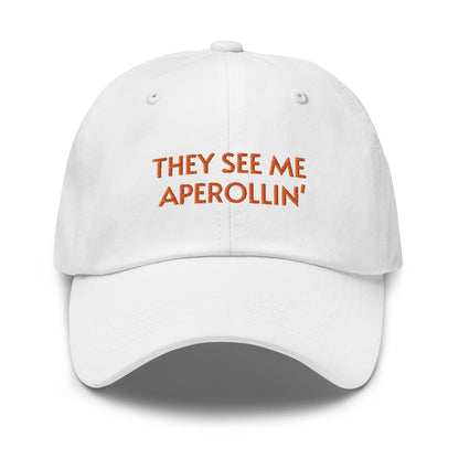 Bild eines Baseball-Caps mit der Bestickung 'They see me Aperolin'' auf weißem Hintergrund. Ein lustiges Accessoire für Aperol-Liebhaber aus 100% Baumwoll-Chino-Cord.