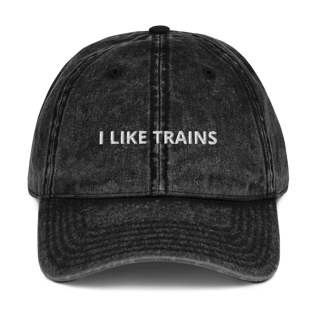 Produktbild der bestickten Vintage-Cap 'I LIKE TRAINS' auf einem weißen Hintergrund. Die Cap besticht durch ihren Vintage-Look und den humorvollen Schriftzug, der die Liebe zum Zugfahren zum Ausdruck bringt.