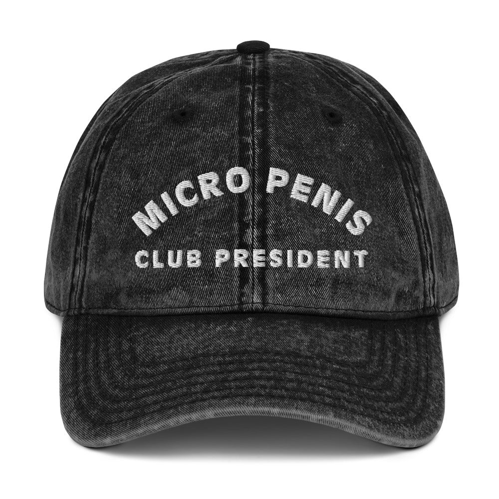 Produktfoto einer Vintage-Cap mit der Aufschrift 'MICRO PENIS CLUB PRESIDENT' auf weißem Hintergrund. Ein humorvolles Accessoire für alle mit Selbstironie.