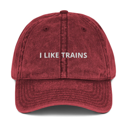 Produktbild der bestickten Vintage-Cap 'I LIKE TRAINS' auf einem weißen Hintergrund. Die Cap besticht durch ihren Vintage-Look und den humorvollen Schriftzug, der die Liebe zum Zugfahren zum Ausdruck bringt.