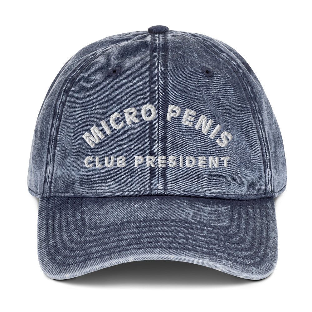 Produktfoto einer Vintage-Cap mit der Aufschrift 'MICRO PENIS CLUB PRESIDENT' auf weißem Hintergrund. Ein humorvolles Accessoire für alle mit Selbstironie.
